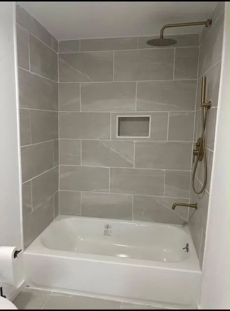 Renovated bathtub and shower with gray wall tile and built-in niche