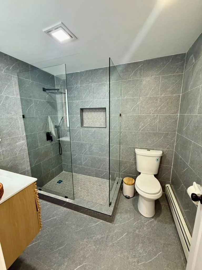 Renovated bathroom with glass-enclosed shower, gray wall tile, and toilet