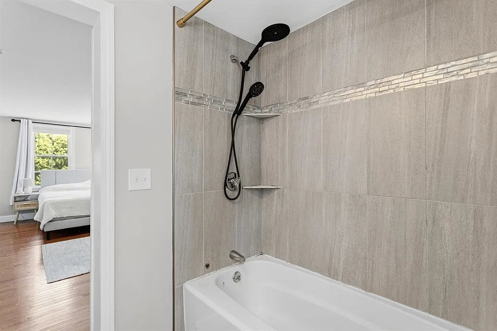 Bathtub and tiled shower with black fixtures beside a bedroom doorway