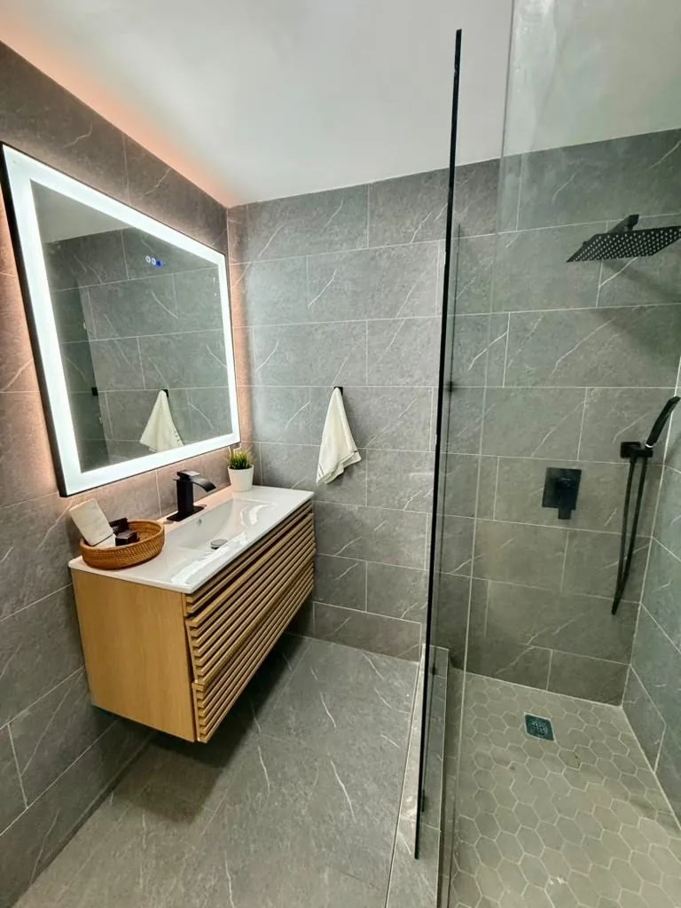 Renovated bathroom with wood vanity, illuminated mirror, and glass-enclosed shower