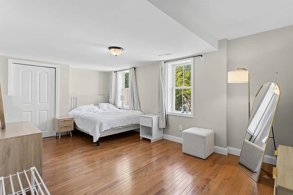 Bright bedroom with wood flooring, two windows, and neutral walls
