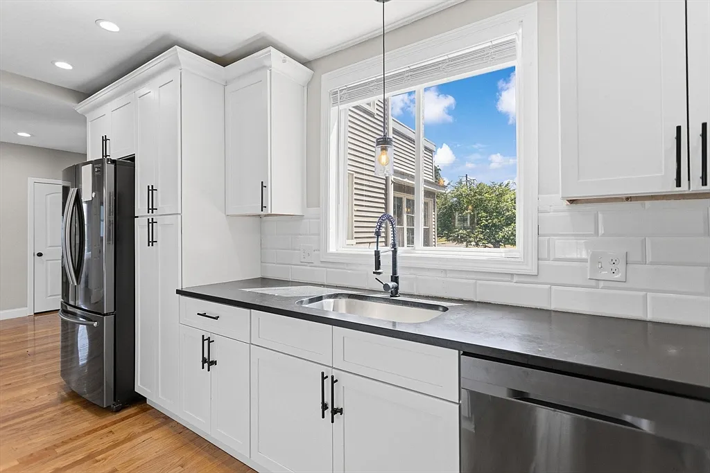White kitchen cabinets with a dark countertop, sink, and black faucet