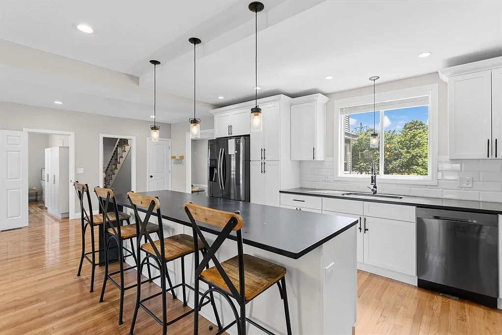 White kitchen with a dark island, pendant lights, and wood flooring
